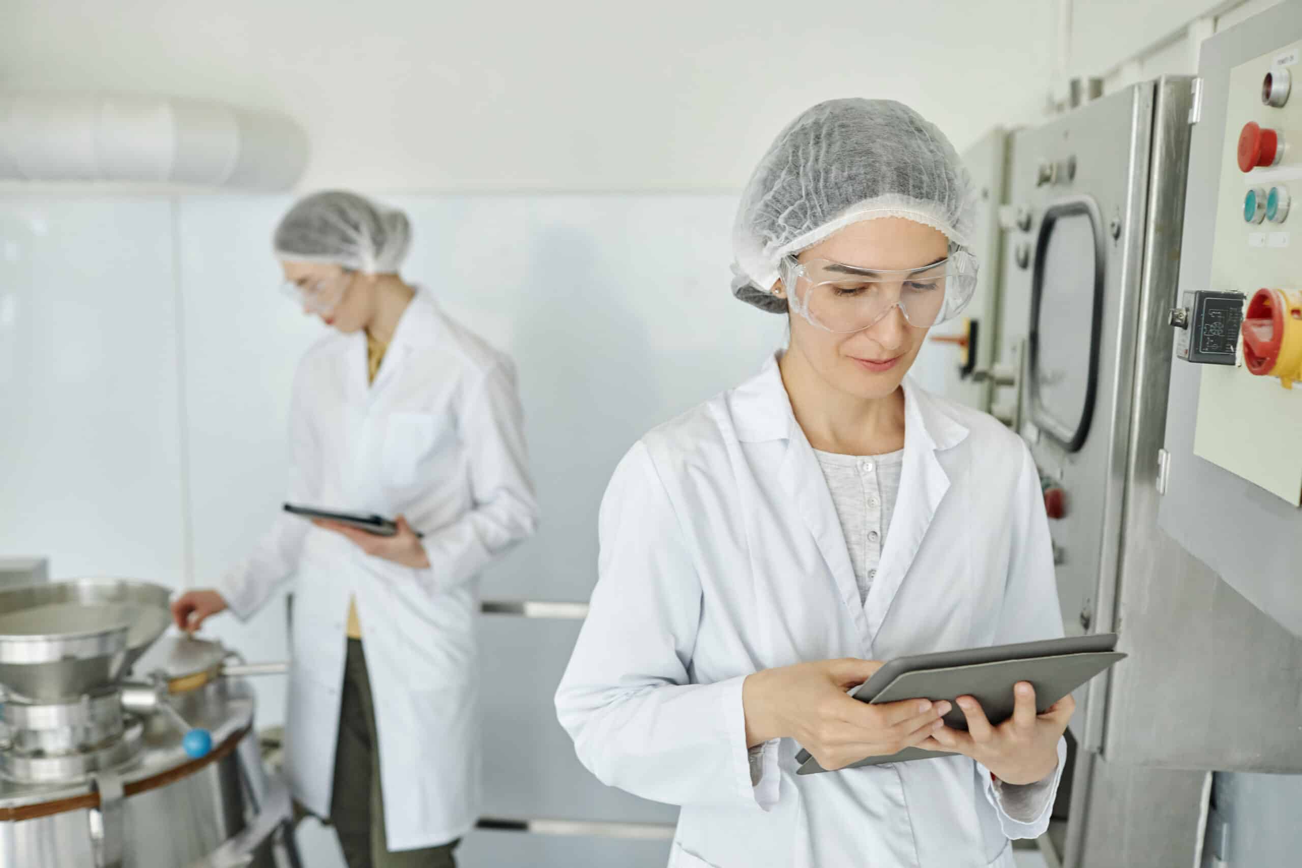 Portrait of two women wearing lab coats working at factory in food or pharma production, copy space