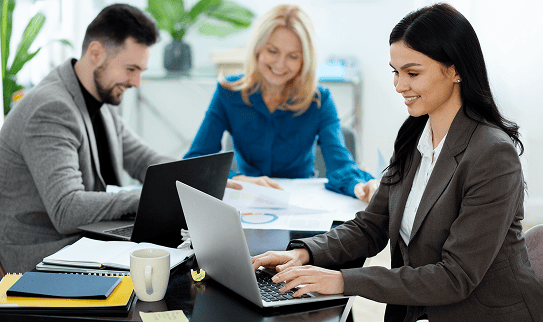 Consultante en ressources humaines travaillant sur ordinateur aux côtés de collègues, illustrant la gestion sociale et l’accompagnement RH global de PG-PS.