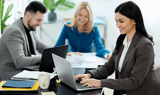 Consultante en ressources humaines travaillant sur ordinateur aux côtés de collègues, illustrant la gestion sociale et l’accompagnement RH global de PG-PS.